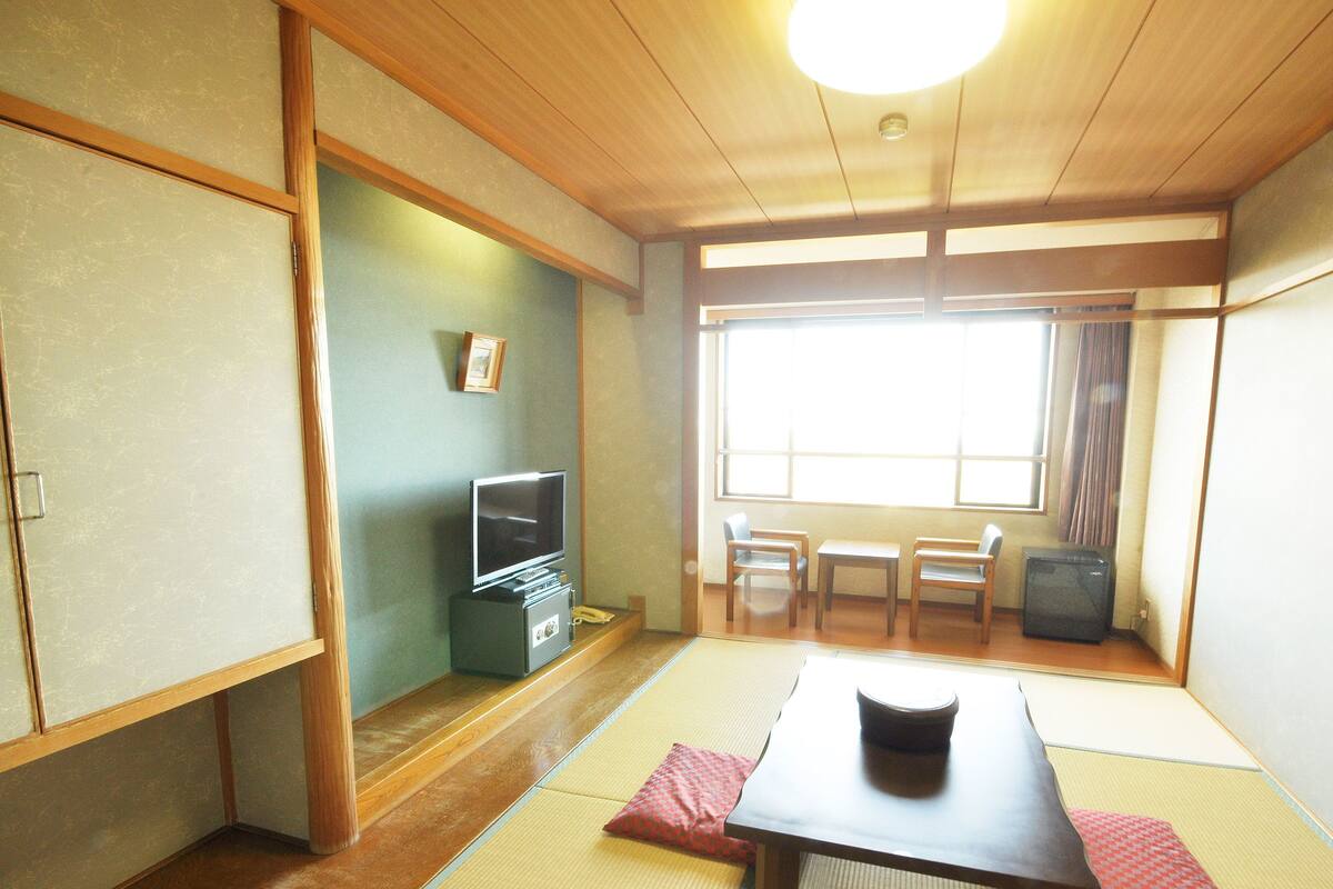 A traditional Japanese room with tatami flooring, a low table, a television, and a small cabinet.