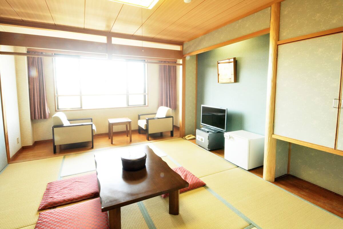 A traditional Japanese room with tatami flooring, a low table with a cat, a television, and a cabinet.