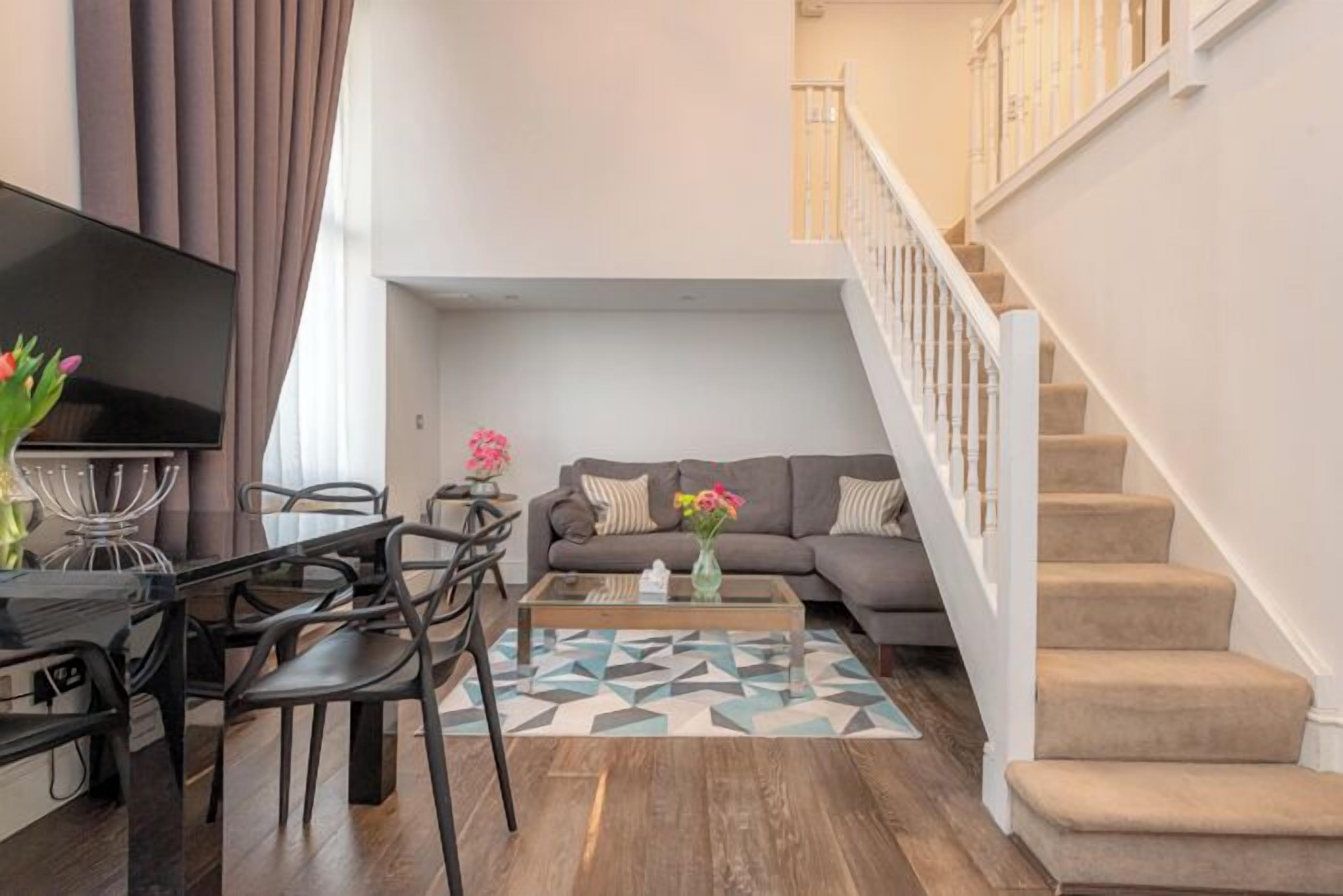 A living room with a sofa, coffee table, and TV, a staircase, and a dining area with chairs and a table.