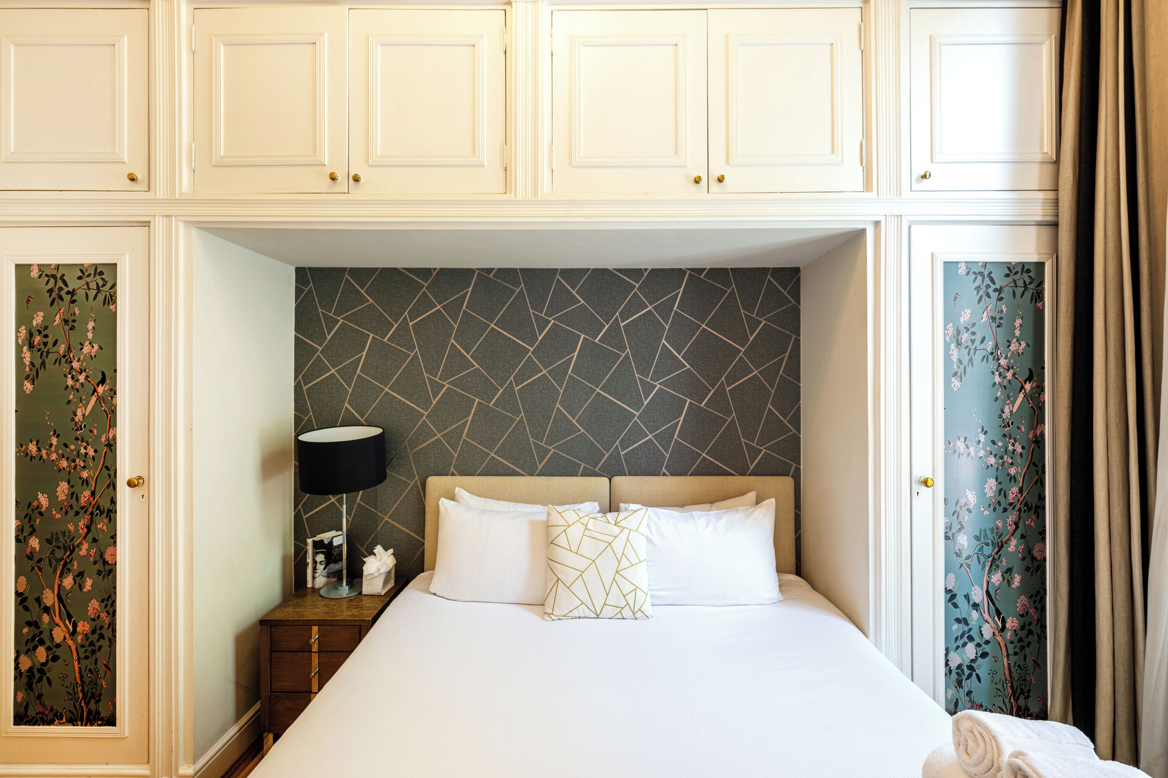 Une chambre d’hôtel avec un lit, une table de chevet et un mur orné d’un motif géométrique.