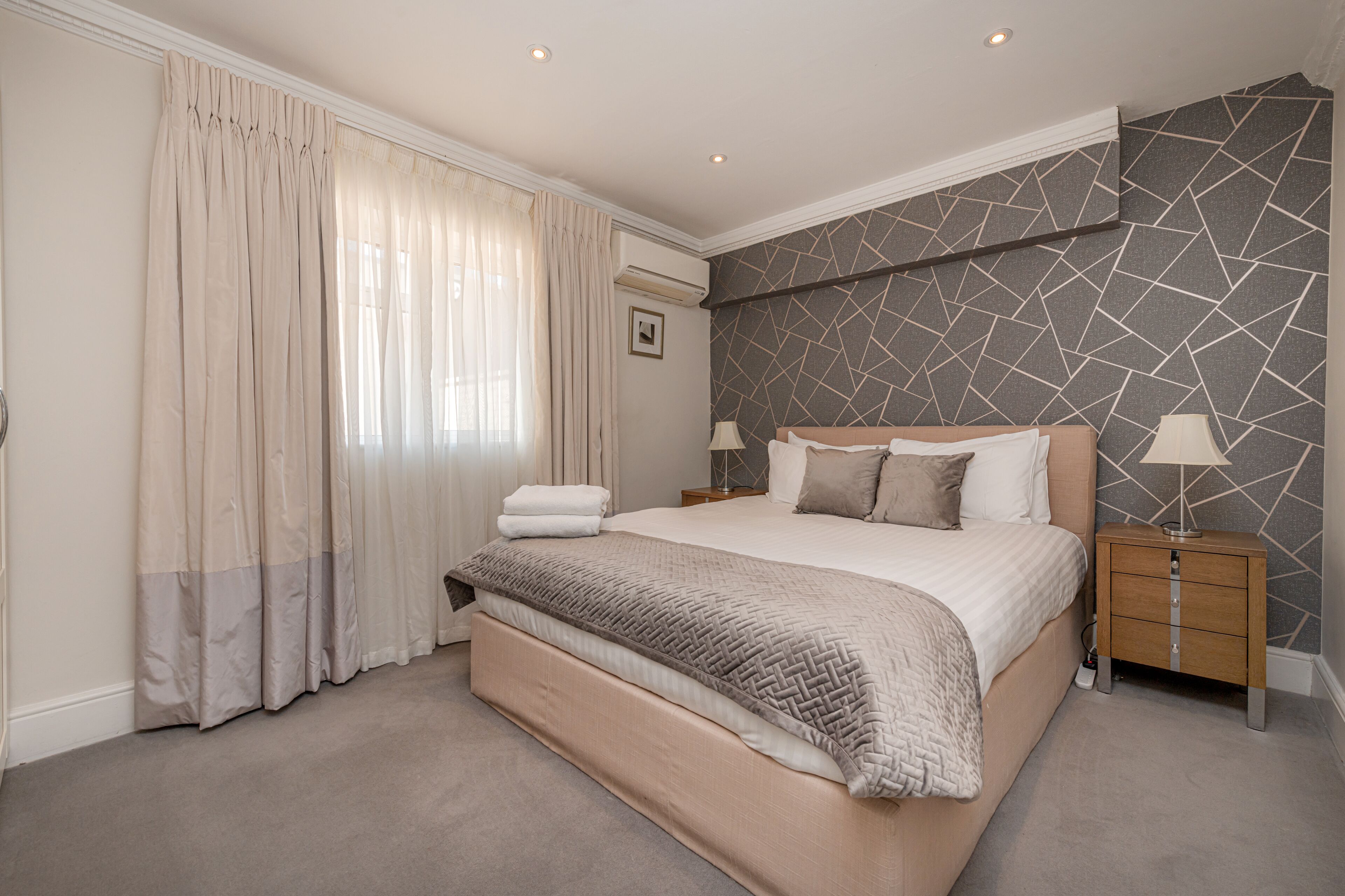 A bedroom with a large bed, a nightstand, a lamp, and a wall with a geometric pattern.