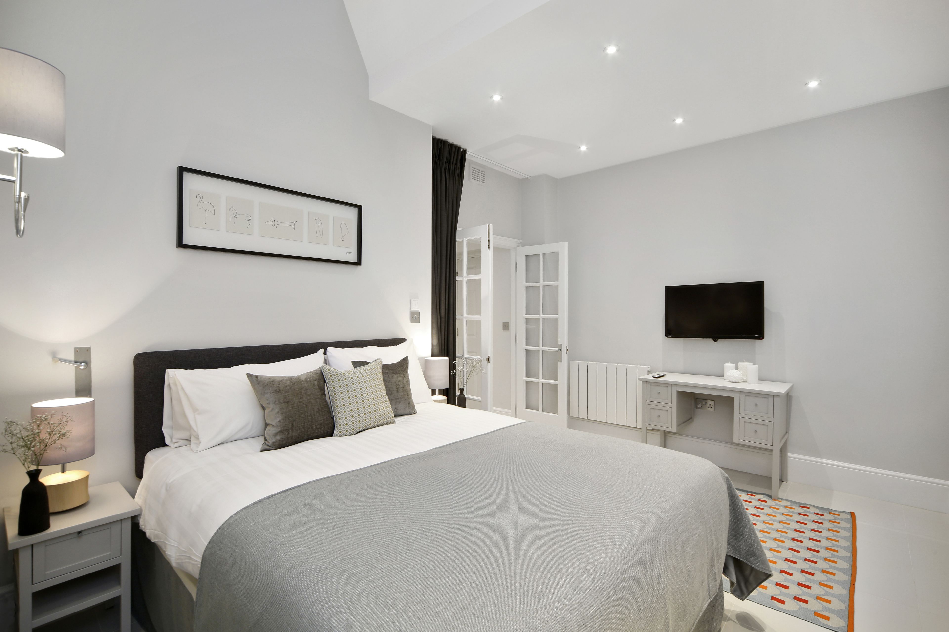 A modern bedroom with a large bed, bedside tables, a desk, and a television.
