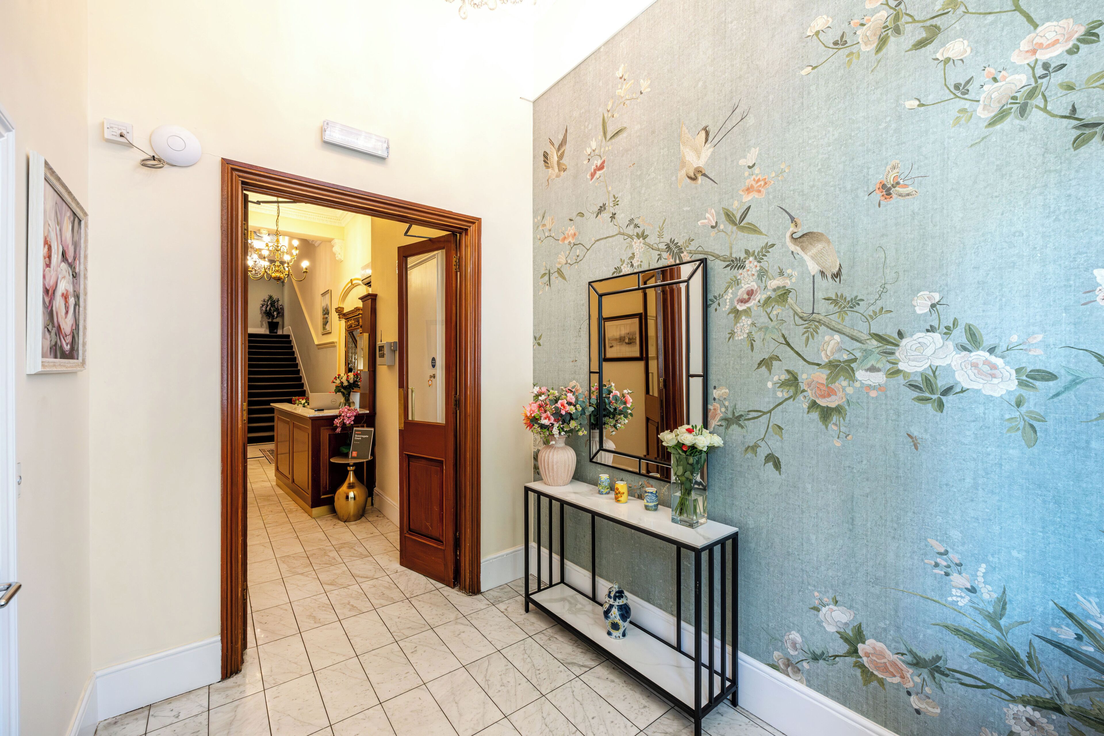 A hallway with a wooden door, a console table with a mirror, and a floral wallpaper.
