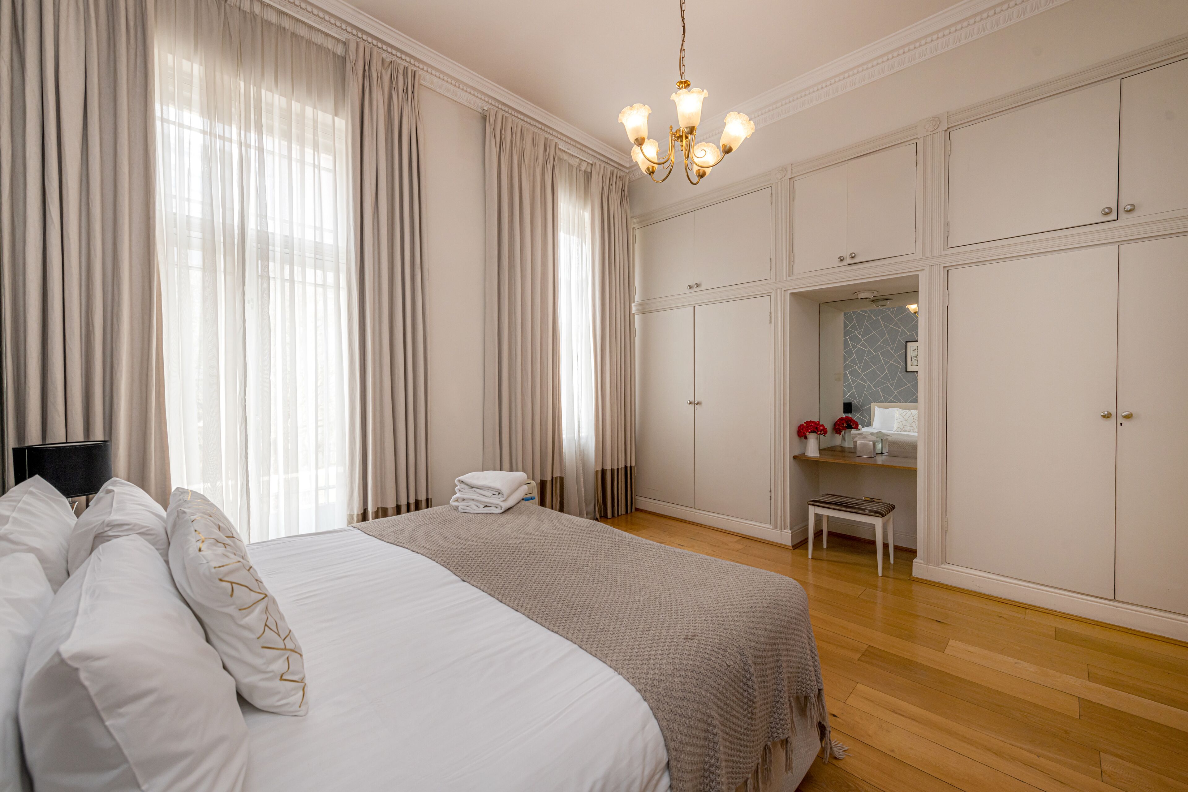 A spacious bedroom with a large bed, a bedside table, a wardrobe, and a chandelier.