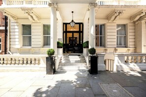 A building entrance with a black door, white columns, and a staircase leading up. - Queensgate Court (London)