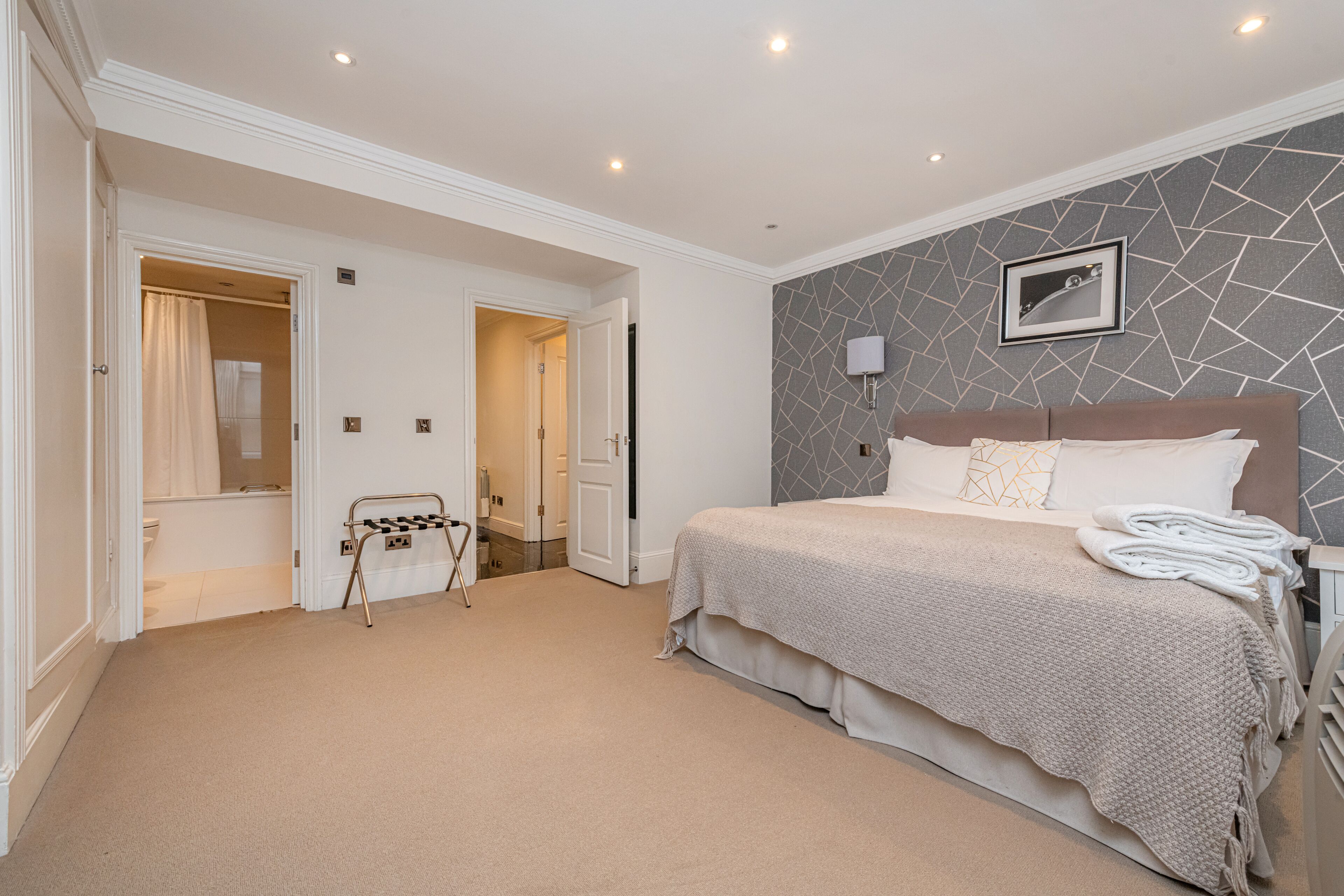 A bedroom with a large bed, a bathroom visible through an open door, and a checkered chair.