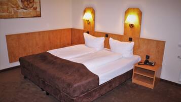 Una habitació d'hotel amb un llit gran, dues làmpades de nit, una tauleta de nit de fusta amb un telèfon i un quadre a la paret.