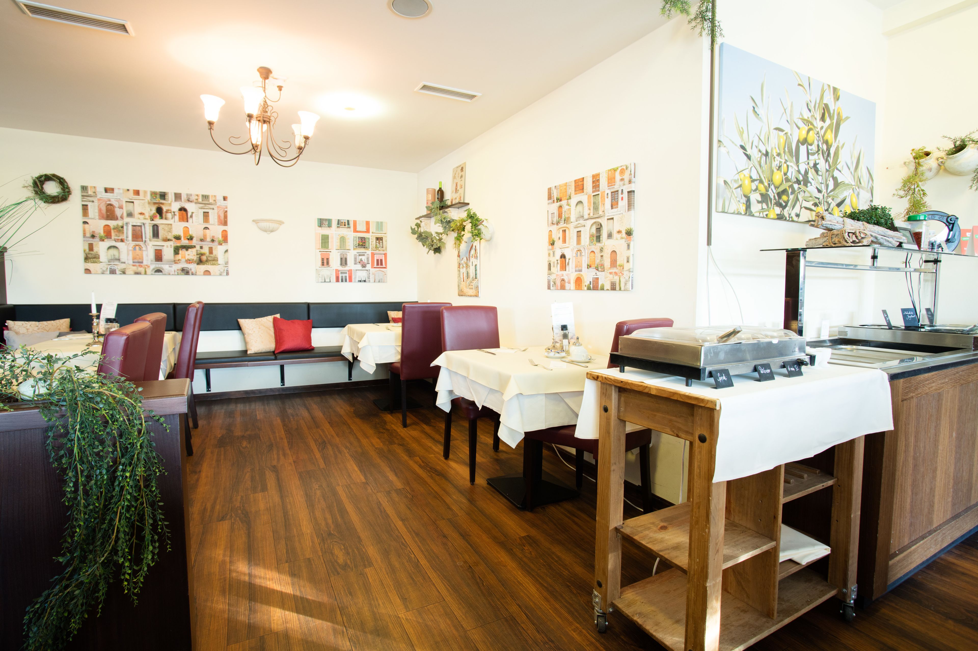 Een restaurant met houten vloeren, rode zachte zitplaatsen, witte tafellaken en een bar in het midden.