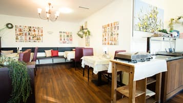Een restaurant met houten vloeren, rode zachte zitplaatsen, witte tafellaken en een bar in het midden.