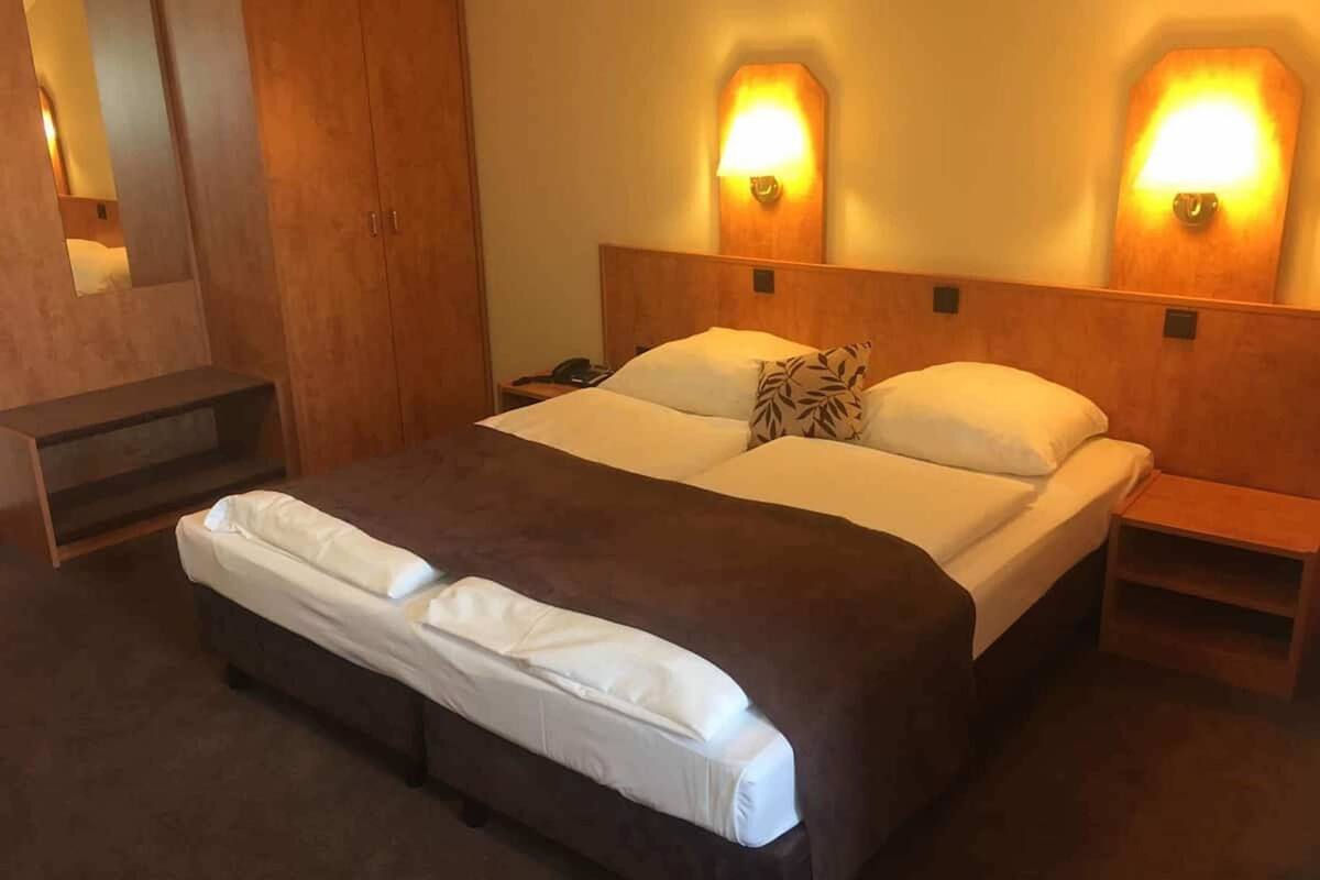 Een hotelkamer met een groot bed, twee bedlampen, een nachtkastje en een houten kledingkast.