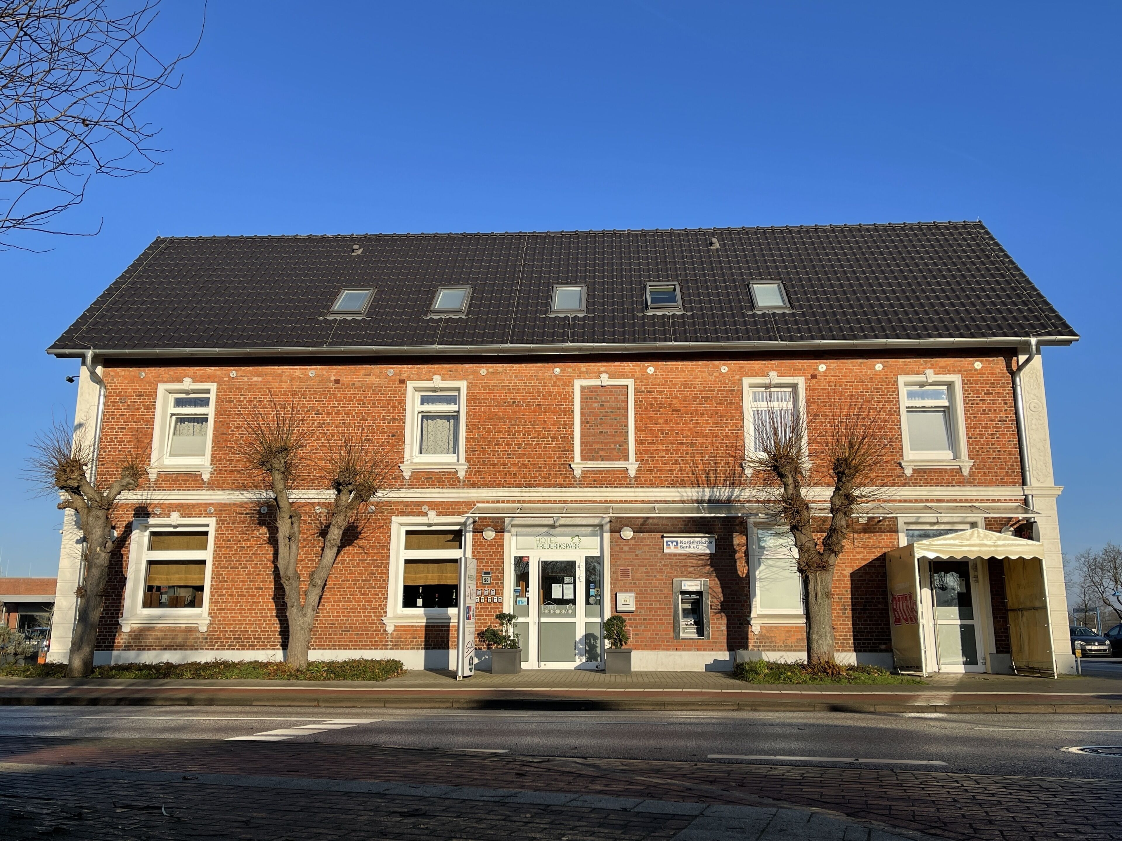 A two-story brick building with a dark tiled roof, multiple windows, and a central entrance.