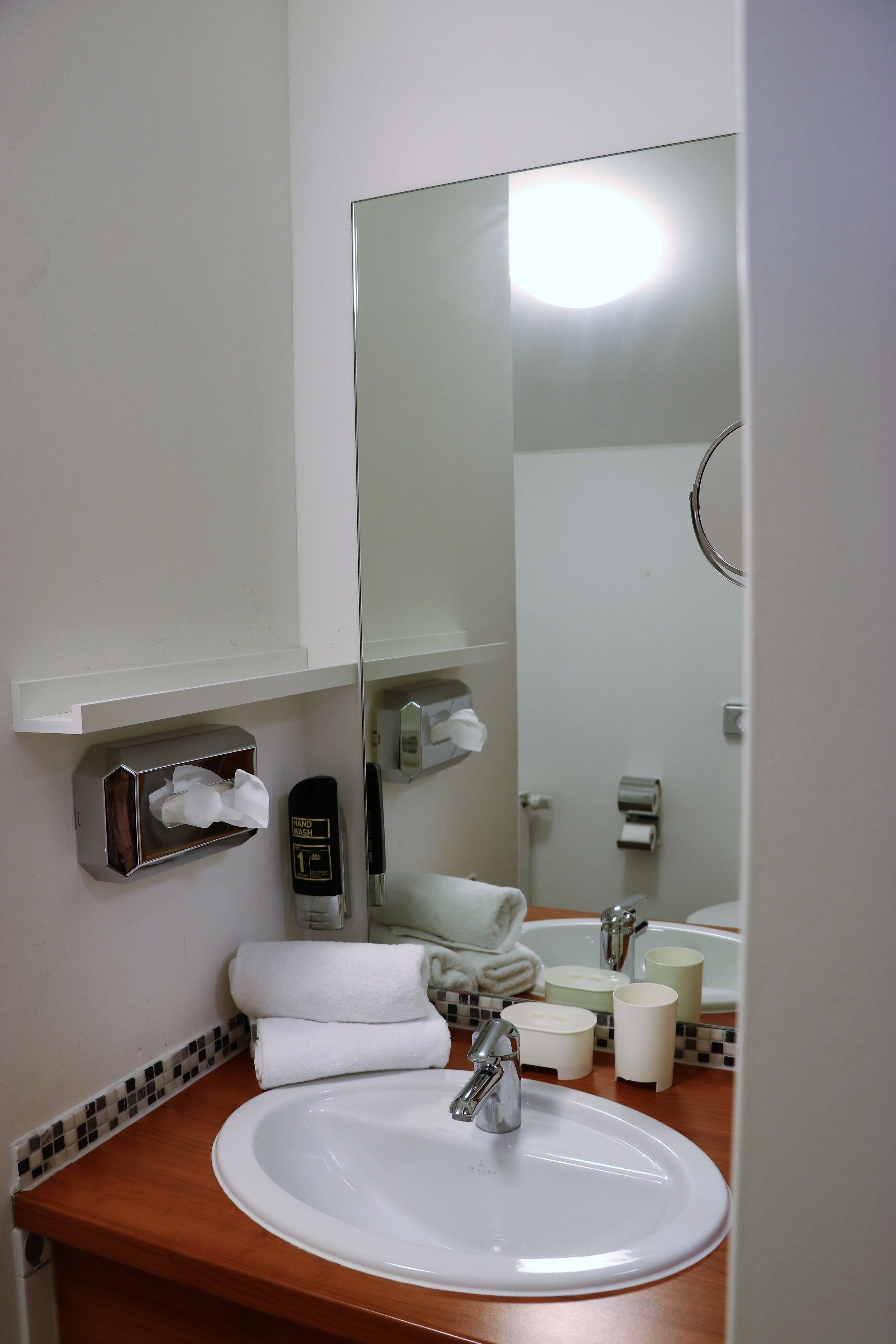 Ein Badezimmer mit Waschbecken, Spiegel, Handtuchspender und Seifenspender.