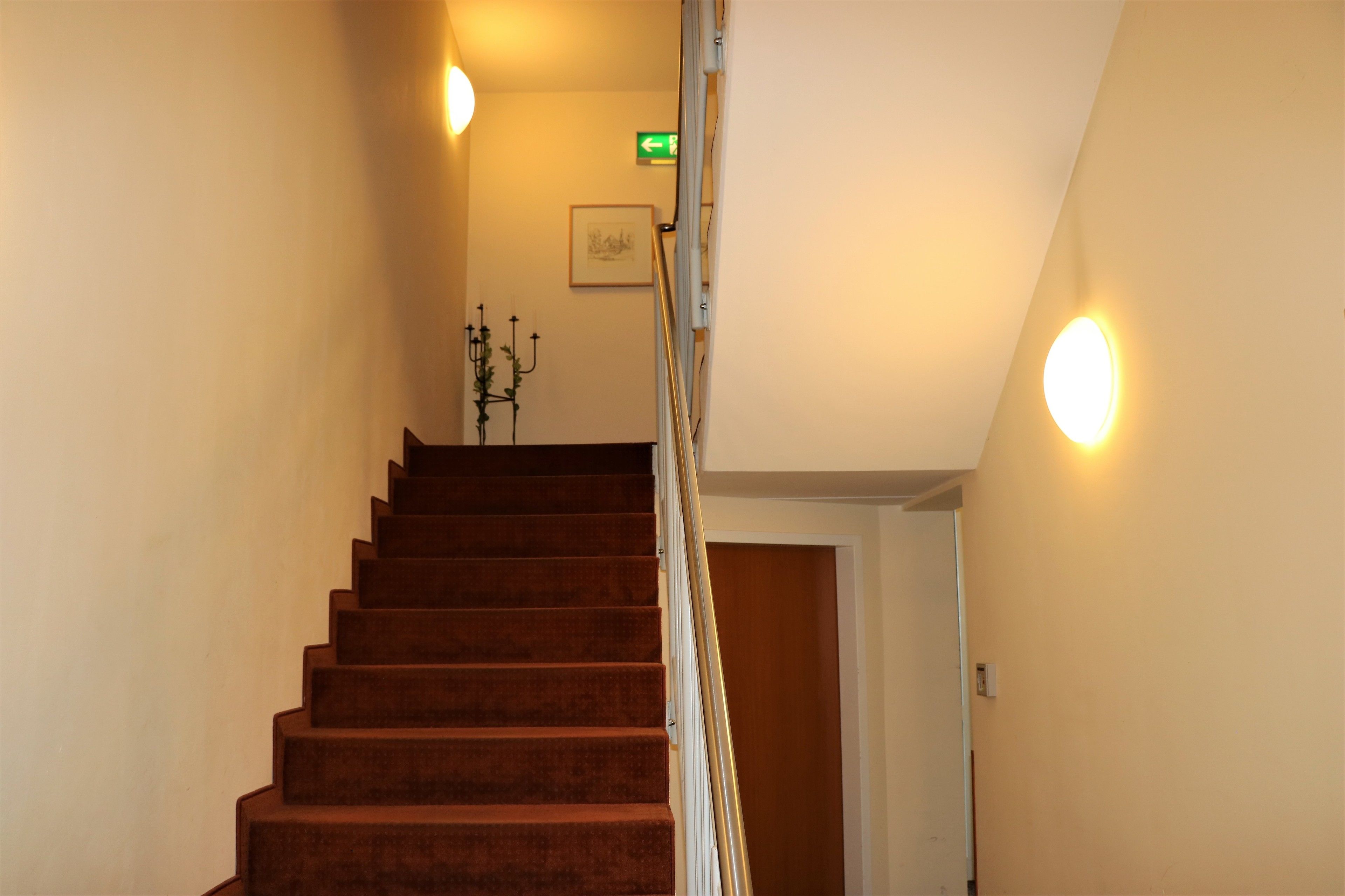A staircase with a handrail, a wall-mounted light, and a framed picture.
