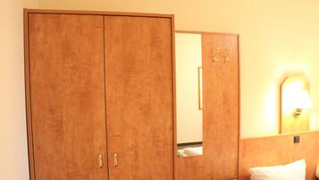 Una camera d'albergo con un armadio in legno, un comodino con una lampada e uno specchio che riflette parte della stanza.