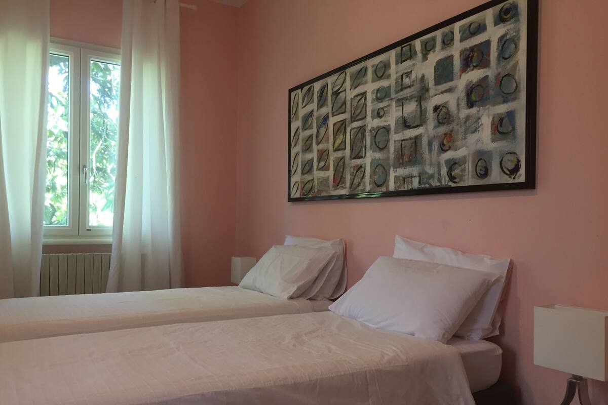 A room with two beds, a window with curtains, and a wall with a framed picture.