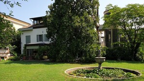 A well-maintained garden with a central fountain, surrounded by lush greenery and a large tree. - B&B Villa al Parco (Sala Baganza)