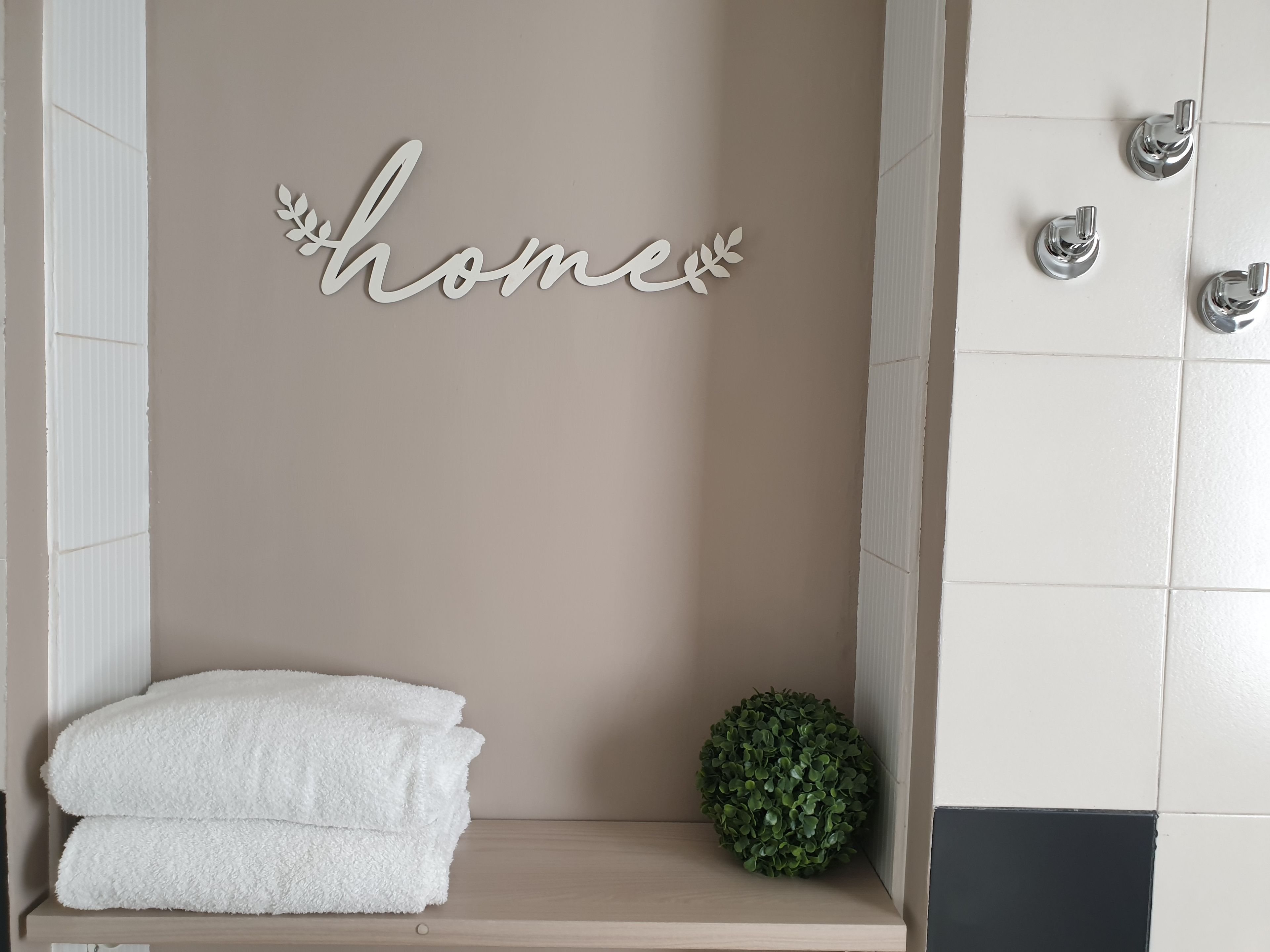Un baño con pared color crema, un perchero blanco y una planta verde pequeña.