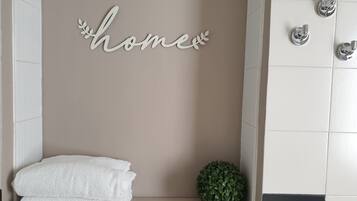 Un baño con pared color crema, un perchero blanco y una planta verde pequeña.
