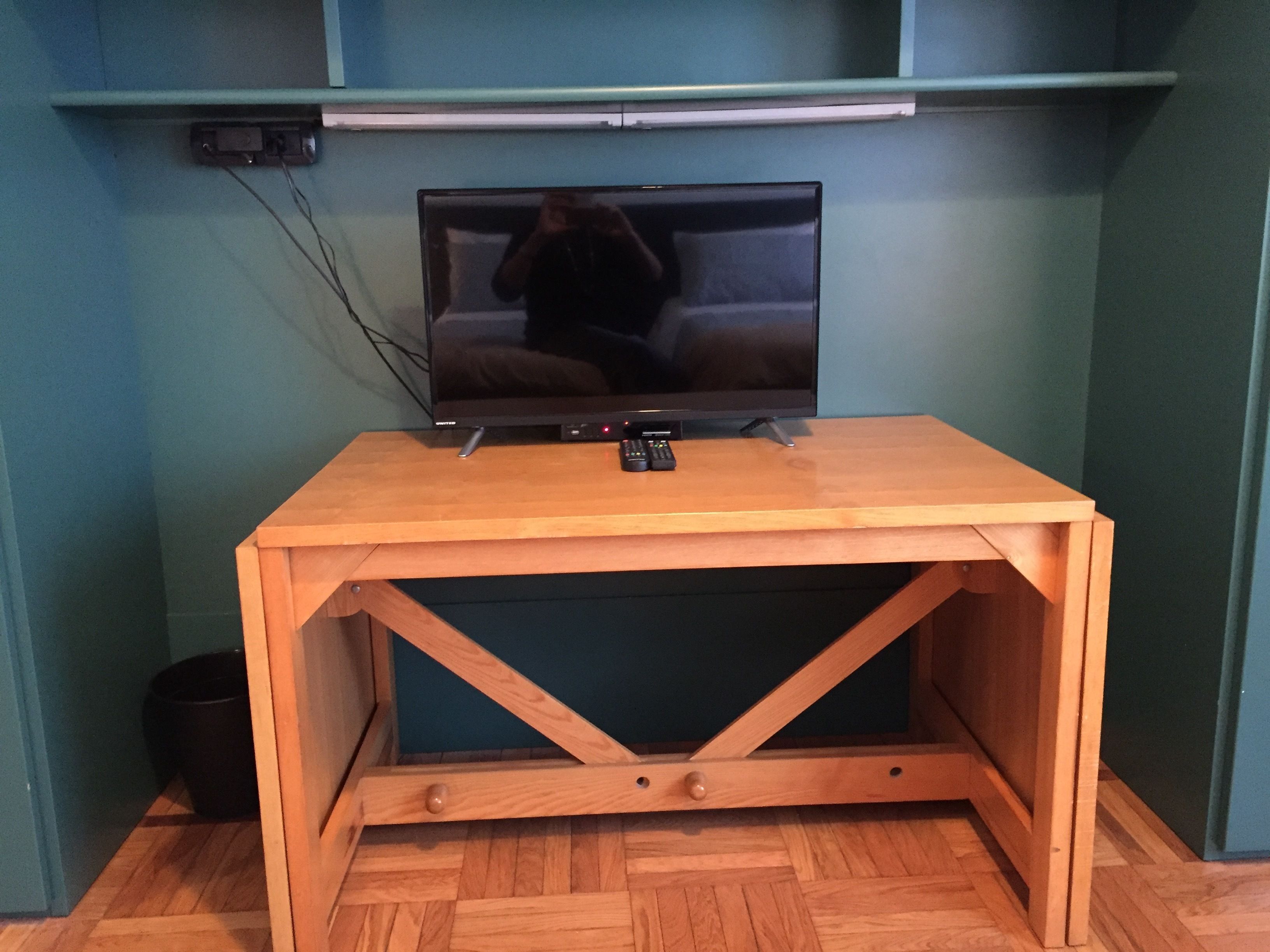 Un meuble en bois pour la télévision, sur lequel est posée une télévision à écran plat, est placé contre un mur de couleur turquoise.