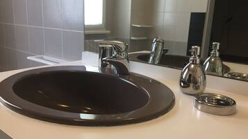 Ein modernes Badezimmer mit einem runden, schwarzen Waschbecken, chromfarbenen Wasserhähnen und einem Spiegel, der Waschbecken und eine Seifenflasche reflektiert.