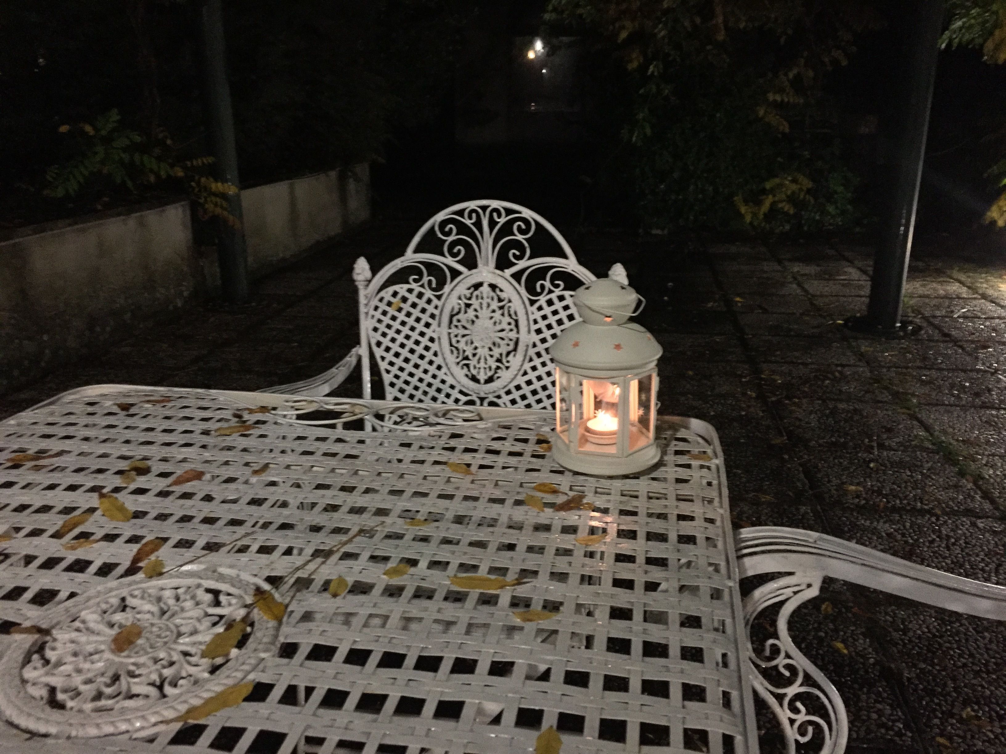 A white metal table with a lantern on it, surrounded by chairs.