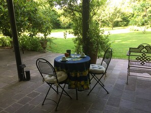A patio with a round table and chairs, surrounded by greenery and a view of a lawn. - B&B Villa al Parco (Sala Baganza)