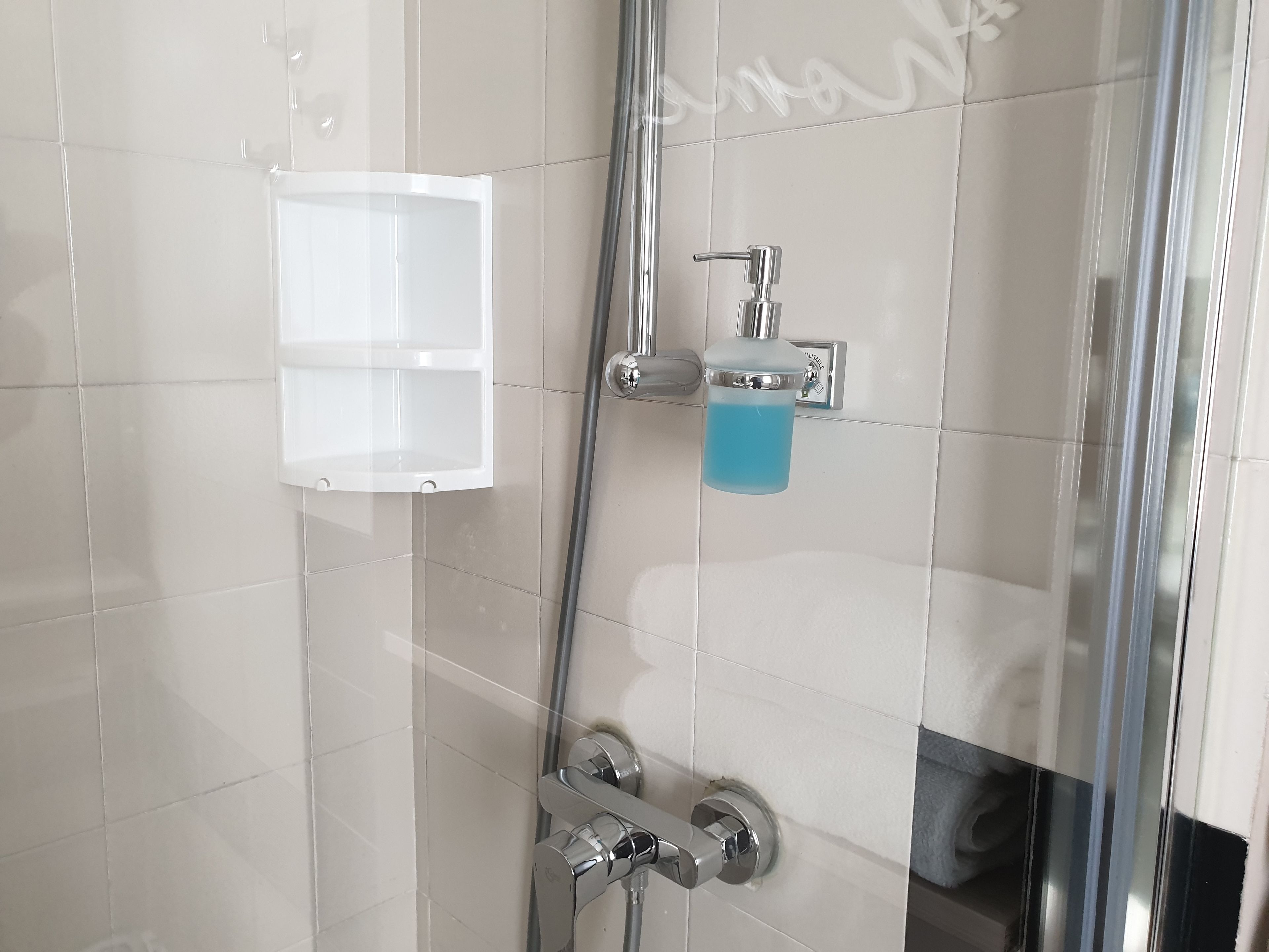 Une salle de bain avec des carreaux blancs, une douche en verre, un robinet chromé et un distributeur de savon.