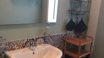 Un baño con un lavamanos blanco, un espejo y una repisa con plantas y un dispensador de pañuelos.