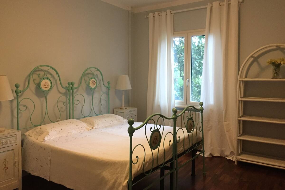 A bedroom with a bed, nightstands, a window with curtains, and a white shelf.