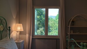 A bedroom with a bed, a nightstand, a lamp, a window with curtains, and a green metal headboard. - B&B Villa al Parco (Sala Baganza)