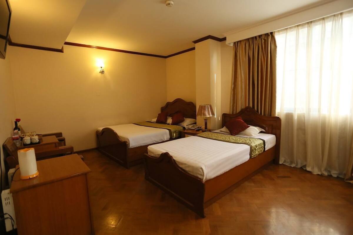 A hotel room with two single beds, a wooden desk, a lamp, and a nightstand.