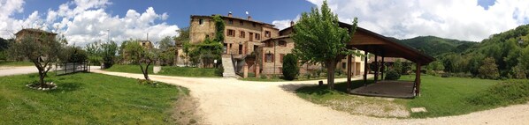 A rustic stone building with a covered outdoor area and a dirt path leading to it. - Agriturismo Le Selve (Comunanza)