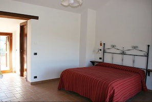 A bedroom with a bed, a nightstand, and a door leading to another room. - Agriturismo Le Selve (Comunanza)