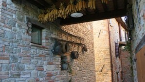 Een smalle stenen gang met hangende trossen bananen en oude metalen bakken aan de muren.