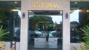 The entrance to a hotel with a glass facade, a sign above the entrance, and a reflection of a car and trees in the glass. - Hotel Suria 18 (Ipoh)
