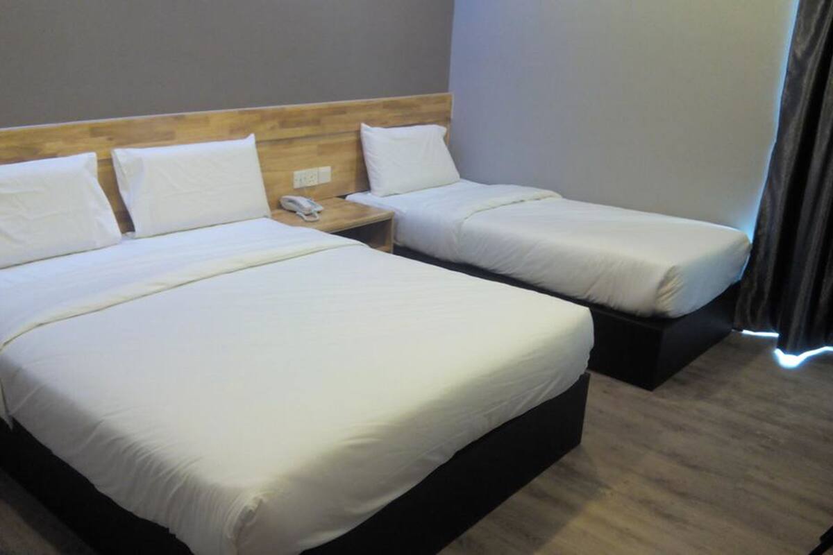 Habitación de hotel con dos camas, cabecero de madera, ropa de cama blanca, mesita de noche con teléfono y ventana con cortinas.