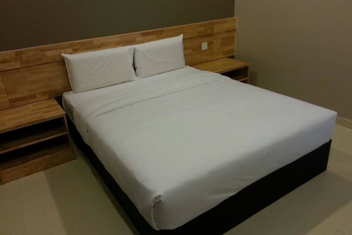 Una cama bien hecha con sábanas blancas en una habitación con cabecera y mesitas de noche de madera.