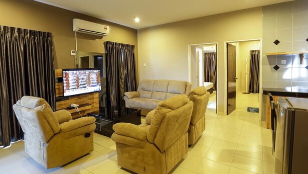 A living room with a sofa set, a TV, and a kitchen area. - Hotel Suria 18 (Ipoh)
