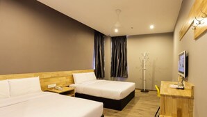A hotel room with two beds, a desk with a computer, a coat stand, and a TV on the wall. - Hotel Suria 18 (Ipoh)