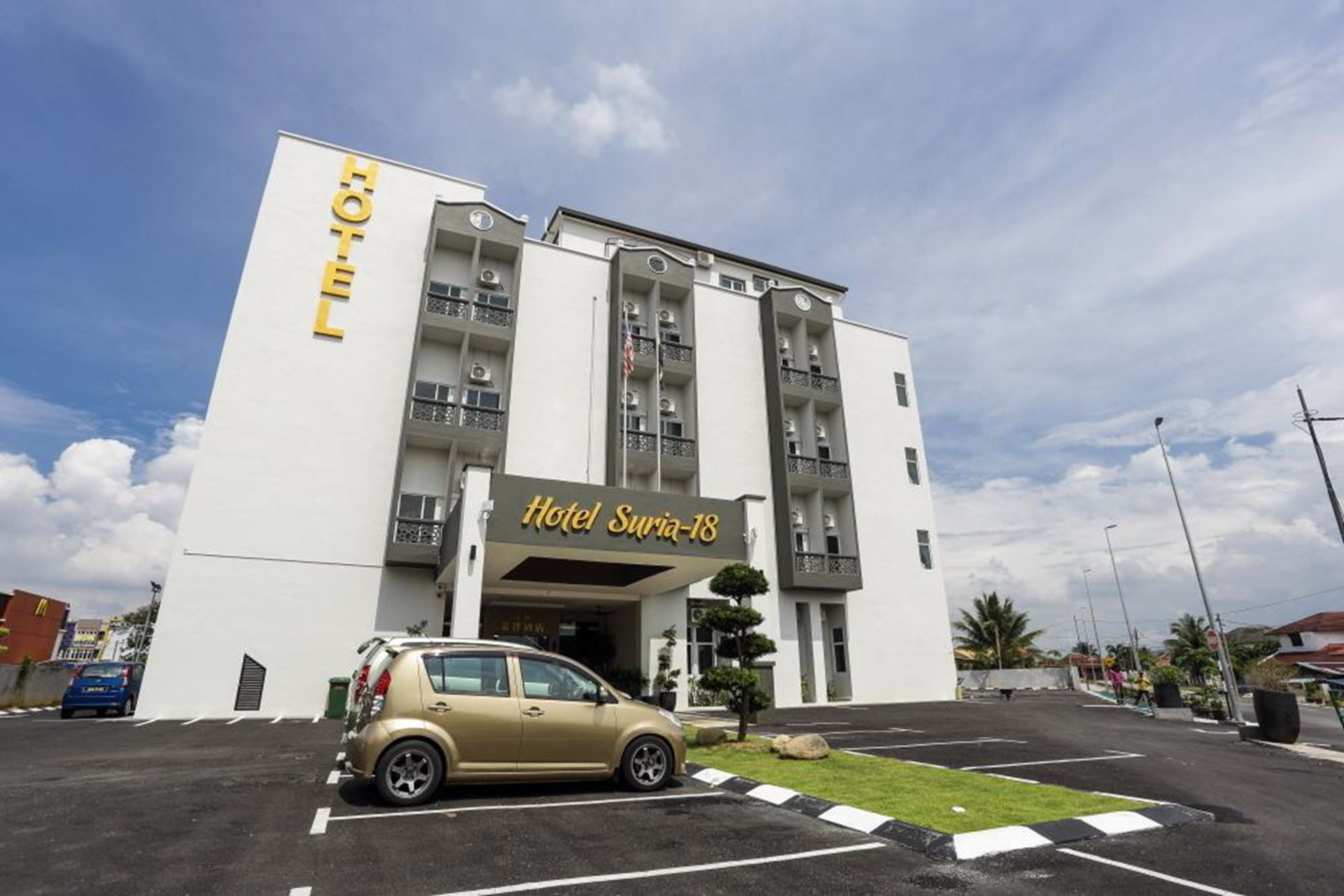 A hotel with a modern facade, a parking lot, and a small car parked in front.