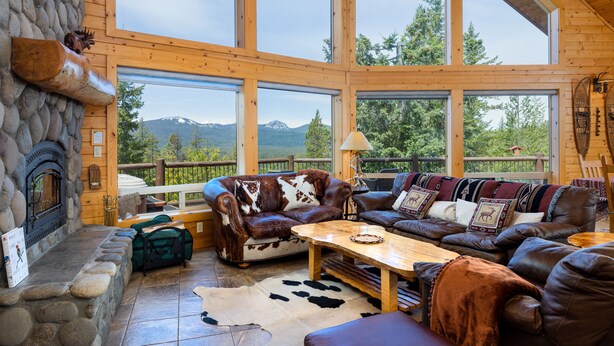 A log cabin interior with a stone fireplace, leather furniture, and large windows offering mountain views. - Luxurious Chalet Retreat: Breathtaking Views, Hot Tub, BBQ, and Fireside Comfort (Crescent)