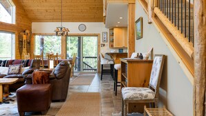 A cozy interior with a wooden staircase, a dining area, and a living room with a sofa and ottoman. - Luxurious Chalet Retreat: Breathtaking Views, Hot Tub, BBQ, and Fireside Comfort (Crescent)