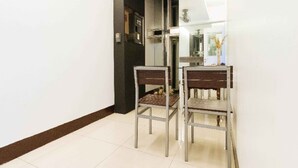 Um corredor com duas cadeiras de metal, uma mesa pequena, uma porta e um espelho na parede.