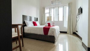 Quarto de hotel com cama, escrivaninha, cadeira, televisão e janela com cortinas.