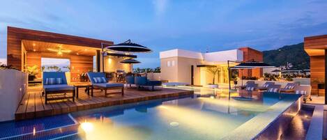 A rooftop pool area with lounge chairs and umbrellas, surrounded by modern buildings.