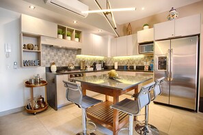 Una cocina moderna con una isla central, electrodomésticos de acero inoxidable y un carrito de servicio de madera de dos niveles.