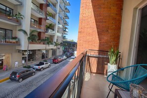 Un balcón con vista a la calle, una silla azul y una planta en maceta.