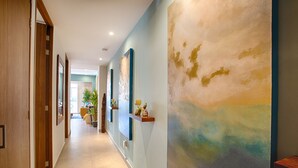 Ein Korridor mit Holztüren, Fliesenboden und einem großen abstrakten Gemälde an der Wand.