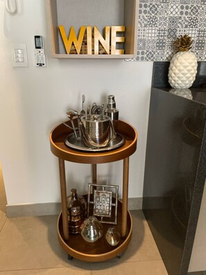 A two-tiered metal tray with glassware and a bottle, set on a wooden stand against a wall with a 'WINE' sign.