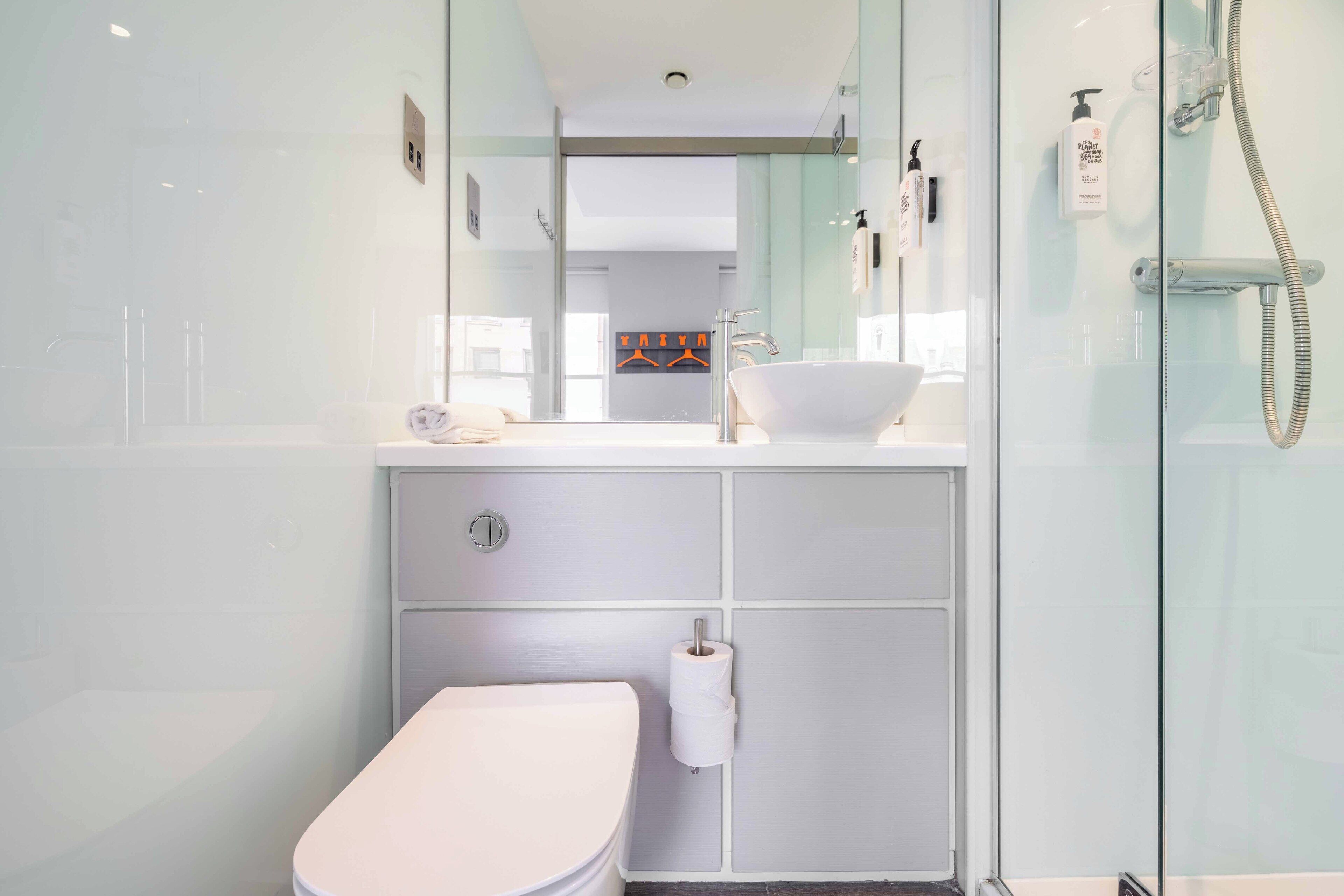 Un baño moderno con cabina de ducha de vidrio, lavabo blanco y retrete.